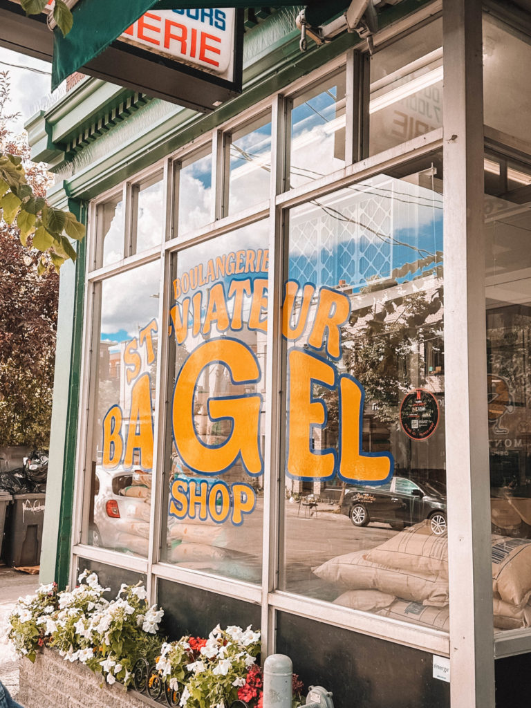 The exterior of St-Viateur Bagel Shop, featuring large, colorful signage on the windows and flower boxes below. This iconic bakery is a recommended stop on any Montreal itinerary for 2 days.