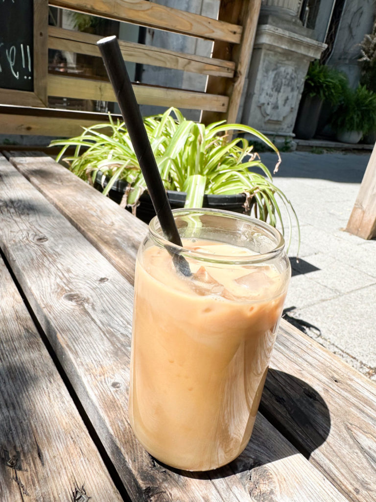 A refreshing iced coffee with a black straw sits on a rustic wooden table in an outdoor setting. This cool drink can be a perfect refreshment spot to include in your Montreal itinerary for 2 days.