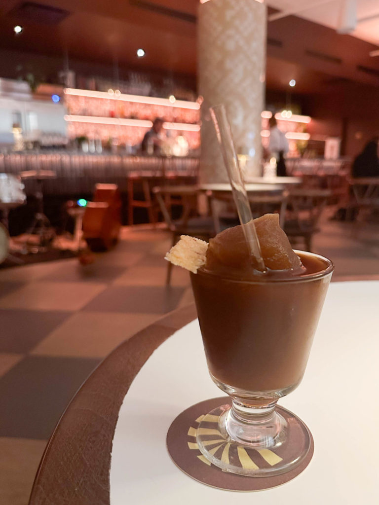 A close-up of an espresso martini garnished with a twist, set against the backdrop of the dimly lit, elegant bar at Le Mal Nécessaire. The exceptional quality of the cocktails at Le Mal Nécessaire might just inspire a return trip to Montreal, adding a special touch to your 2-day itinerary.